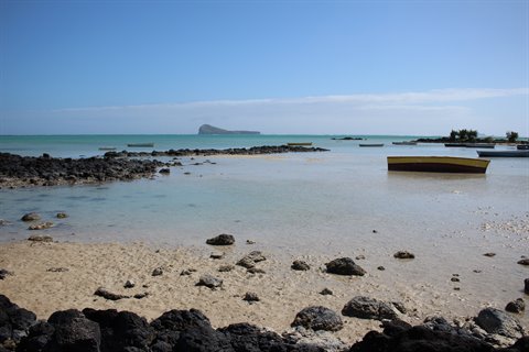 Yellow boat stranded on rocky beach, volcanic island on horizon, bright daylight