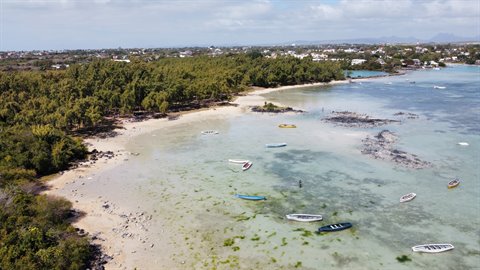 Boat seen from above on turquoise lagoon with seaweed, sandy beach and tropical trees around