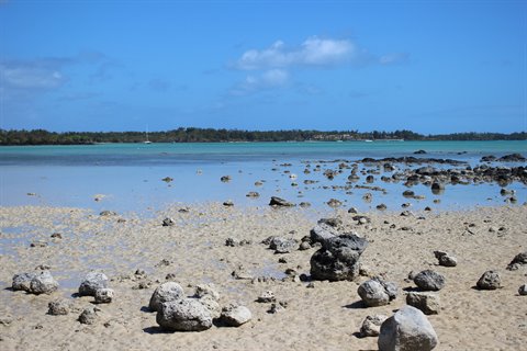 Volcanic rocks on sandy beach with turquoise lagoon and blue sky