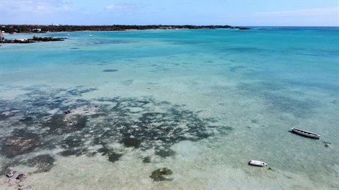 Clear turquoise waters with two anchored boats near the shaded coastline
