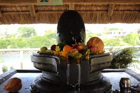 Black stone altar with fruit and flower offerings, natural daylight, open-air shrine