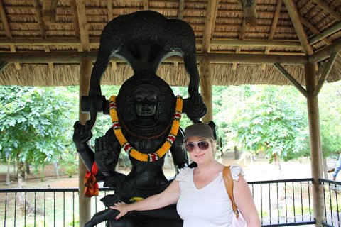 Tourist under a wooden pavilion beside a stone statue with flower garlands
