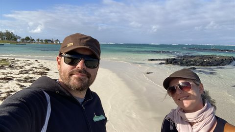 Couple in caps and sunglasses taking selfie on white sand beach, daylight