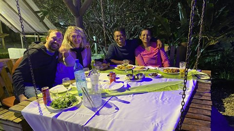 Four smiling friends dine together at an outdoor table, lit by night flash
