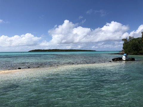 Turquoise lagoon with green islet in background, small boat on sandy shallows, bright sunlight