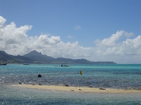 Turquoise lagoon with boats, mountains in background and sandy shore in foreground
