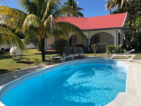 Blue pool in front of villa with red roof, palm trees and sun loungers