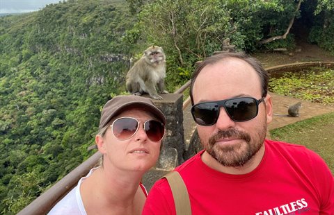 Couple in sunglasses takes a selfie, monkey on a stone pillar, green tropical forest