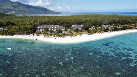 Tropical beach with hotel among trees, turquoise coral reef, bright daylight