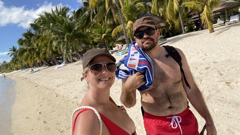 Couple taking selfie on sunny tropical beach, palm trees and white sand, man holding towel