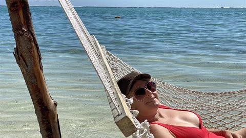 Woman in sunglasses and hat relaxing in a hammock on the beach, turquoise sea