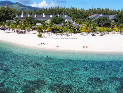 White sand beach and turquoise sea in front of a resort with palm trees, midday light