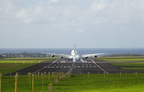 Four-engine jet taking off from runway, smoke under wheels, green grass, soft light