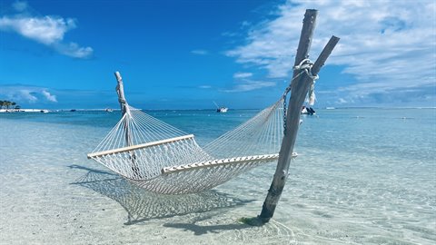 White rope hammock tied to wooden poles in crystal-clear shallow water