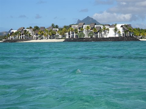 Turquoise sea in front of white resorts with palms and mountain, daylight