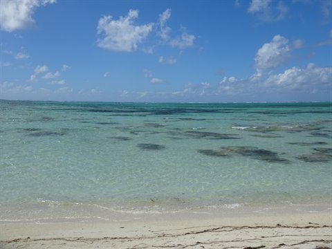 Clear turquoise water over reef, pale sand and blue sky with clouds