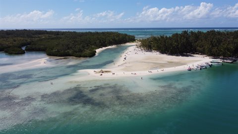 White sand between turquoise lagoon and green trees, anchored boats, people walking