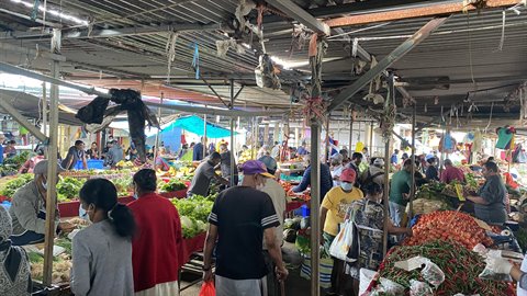 Masked visitors browse vegetable stalls in a busy covered market hall