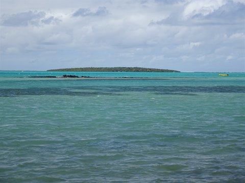 Green islet surrounded by turquoise sea under a cloudy sky, travel journal