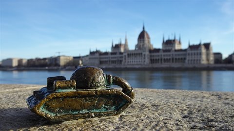 Small bronze tank figurine on stone, blurred parliament building across the river