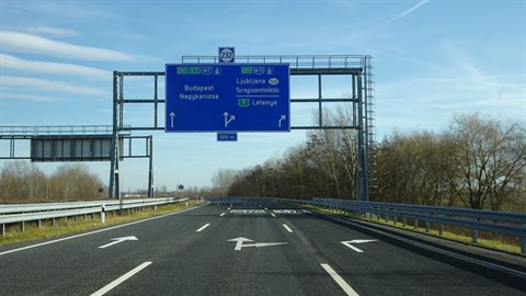 Blue highway sign above an empty road, bare trees, clear sky