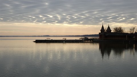 Pier and turreted building by the lake, streaked clouds reflected in calm water
