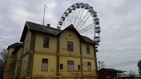 Metal Ferris wheel behind an old abandoned yellow building, cloudy sky