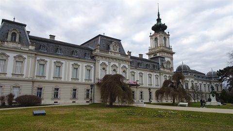 Baroque palace facade with green tower, front lawn, diffused cloudy light, visitors walking