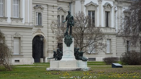 Bronze statue on pedestal in front of historic palace, soft light, bare trees