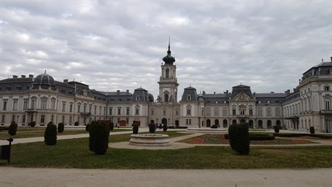 Baroque palace with formal garden and clipped shrubs, under cloudy sky