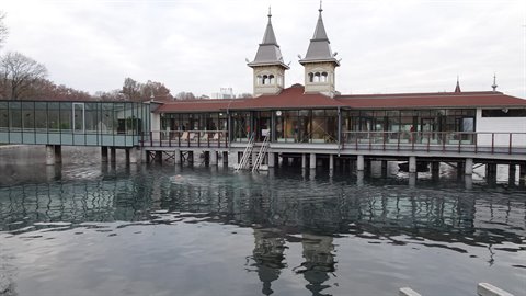 Historic pavilion with towers on a thermal lake, dark water and grey sky