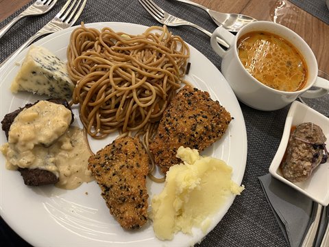Plate of spaghetti, blue cheese, meat and mashed potatoes with soup, cutlery on table