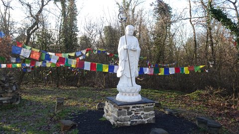 White stone Buddha statue among colorful prayer flags and bare trees, daylight