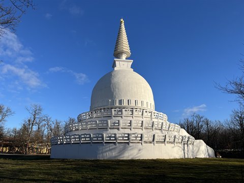 White stupa under blue sky, bare trees, bright sunlight