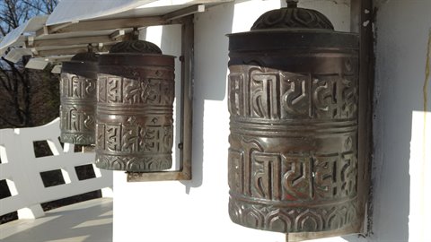 Engraved metal prayer wheels on a white wall, direct sunlight, travel journal