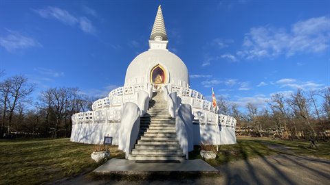 White stupa with staircase and golden statue, bare trees, blue sky with clouds