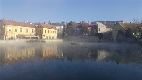 Colorful houses reflected in a misty lake, golden morning light