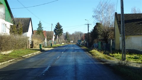 Asphalt road between low houses and fences, blue sky, winter sunlight