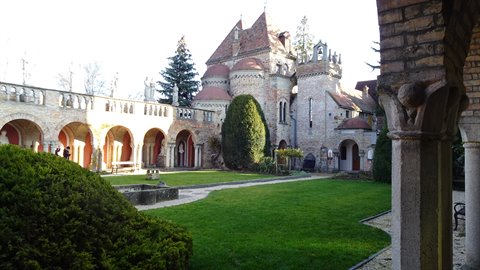 Stone castle with arches and towers, green lawn, daylight, framed by columns