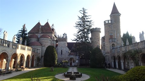 Stone castle courtyard with conical towers, garden and central fountain, daylight