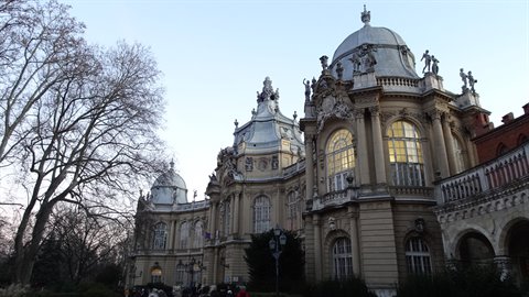 Historic domed palace with statues, softly lit, beside bare trees at dusk