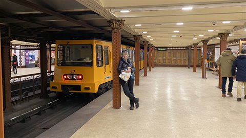 Traveler leaning on a column next to a stopped yellow subway train