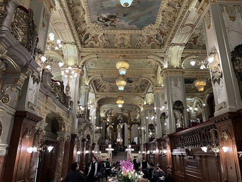 Historic hall with frescoed ceiling, golden chandeliers and café guests, warm light