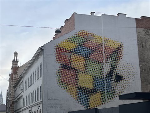 Colorful mural of circular patterns on white building facade, historic architecture nearby, daylight