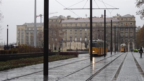 Yellow tram on wet tracks, gray historic buildings under cloudy sky