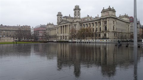 Historic palace with towers reflected on the rain-soaked square under gray sky