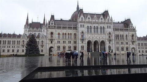Tourists with umbrellas in front of the neo-Gothic parliament building, wet square, grey sky