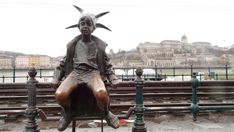 Bronze statue of a little girl sitting on a railing, palace on the hill behind