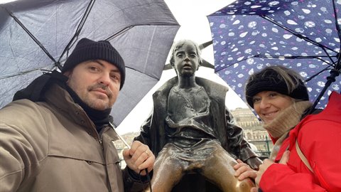 Couple under umbrellas beside child statue, soft daylight