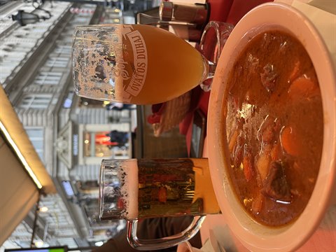 Goulash soup and beer on restaurant table, blurred historic buildings in urban background